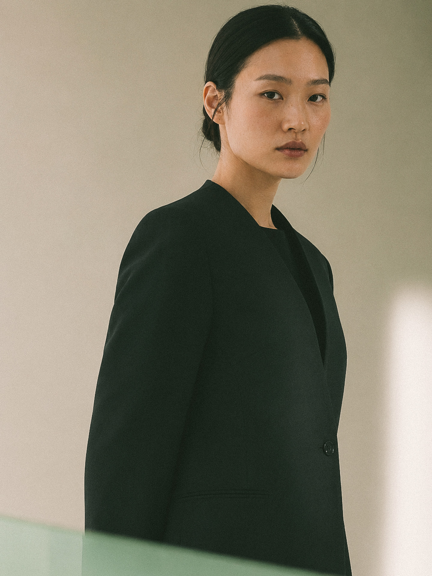 Collarless uniform jacket in black wool, worn in three-quarter view